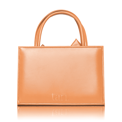 back of camel colored rectangular purse with a prominent bow accent and sturdy top handles.
