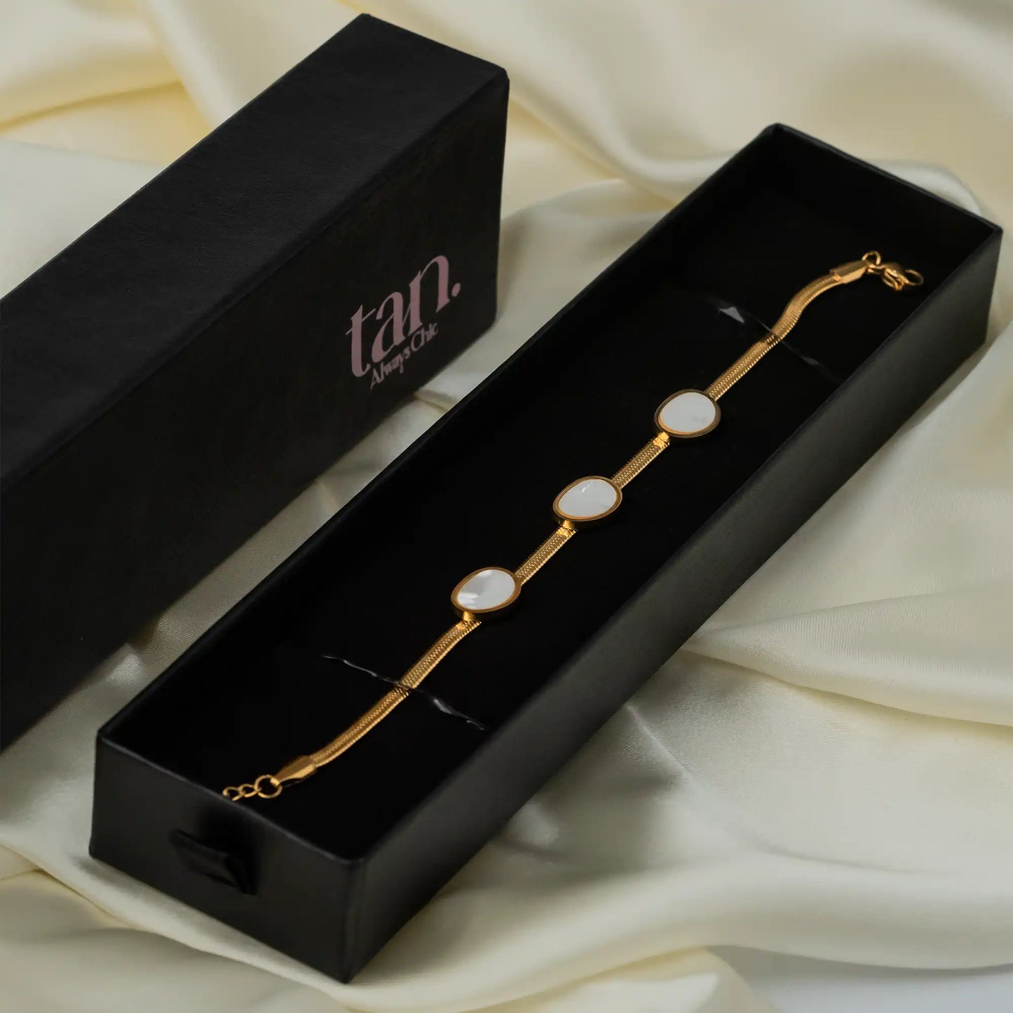 Gold snake chain bracelet with oval white shell insets in a black Tan gift box